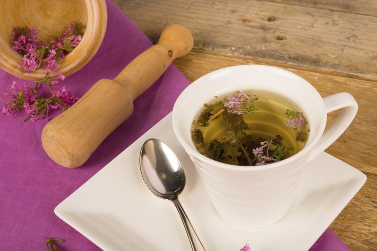 Las flores de valeriana en un bol de madera junto a una taza de té de valeriana caliente.