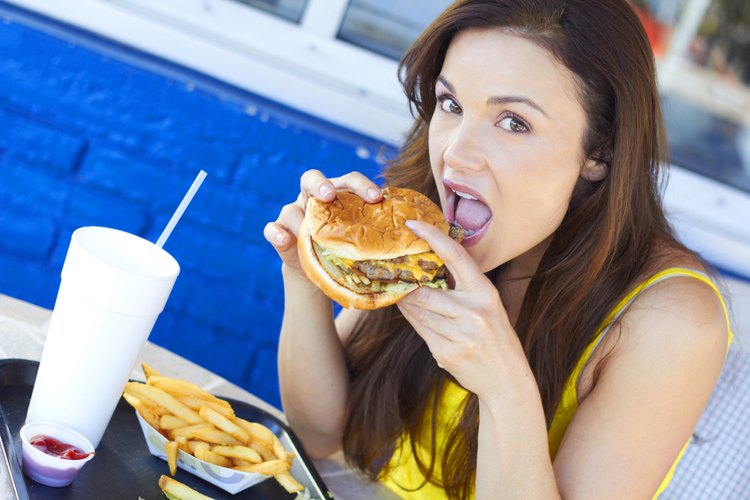 Mujer joven comiendo una hamburguesa con papas fritas.