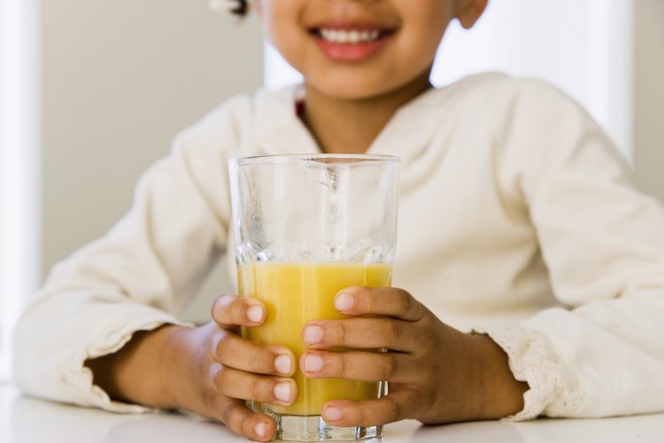Niña pequeña bebe un vaso de jugo de naranja.