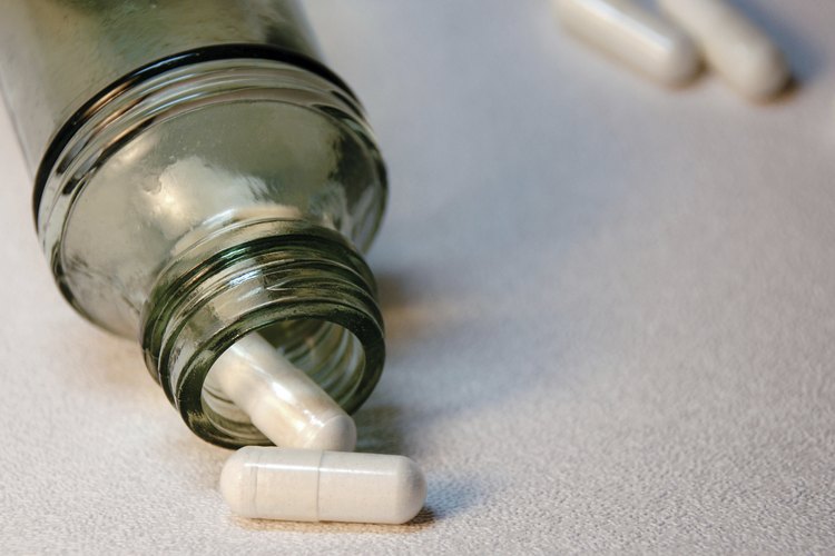 Cápsulas blancas se derraman fuera de una botella de vidrio sobre papel blanco.