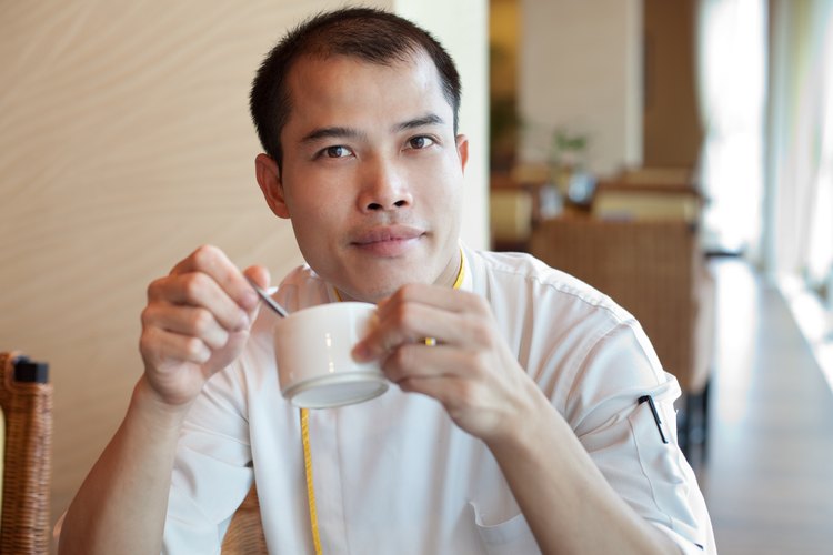 Hombre calvo que sostiene una taza de café.