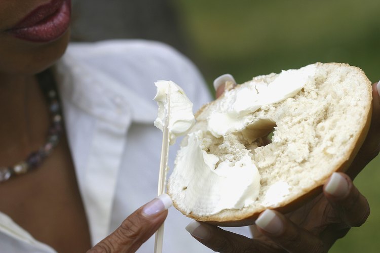 Mujer esparciendo queso crema sobre un bagel.