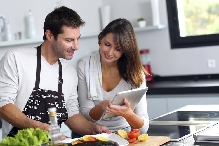 Pareja en la cocina usando una tablet para hacer la cena.