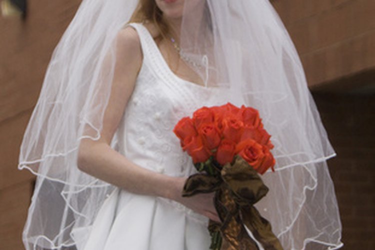 Novia tradicional con vestido blanco y velo, con un ramo de rosas rojas.