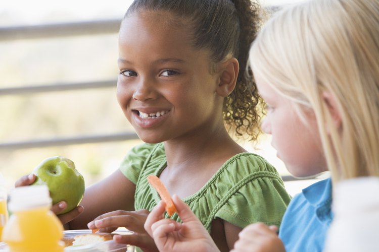 Niñas comiendo manzana y zanahoria en la escuela.