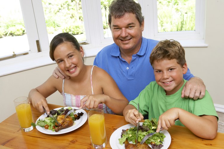 Padre que prepara pollo y ensalada para sus hijos.