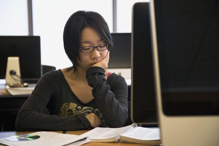 Estudiante leyendo libros frente a una computadora