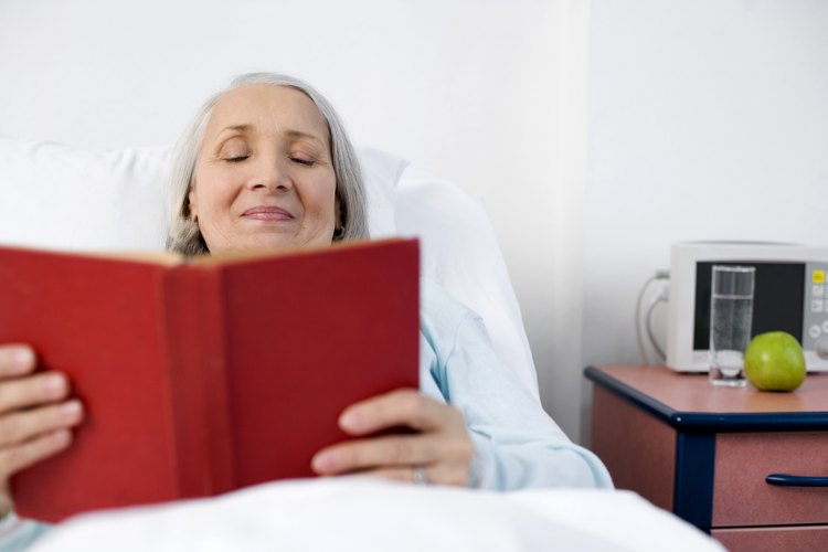Mujer mayor leyendo un libro en la cama.