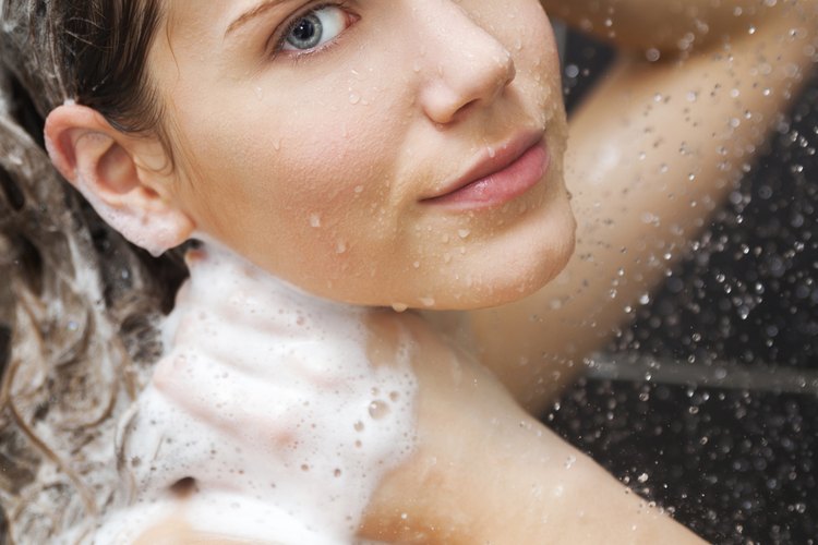 Una mujer sonriente, duchándose y lavando su cabello.