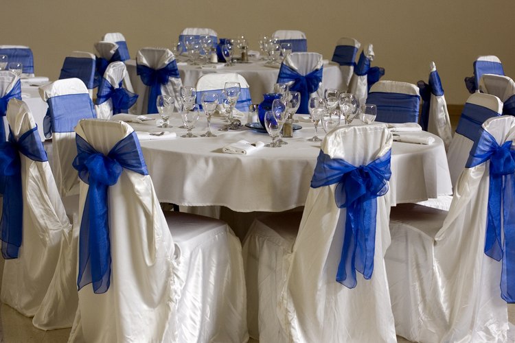 La decoración incluye moños azules de tul amarrados sobre el cubresillas blanco.