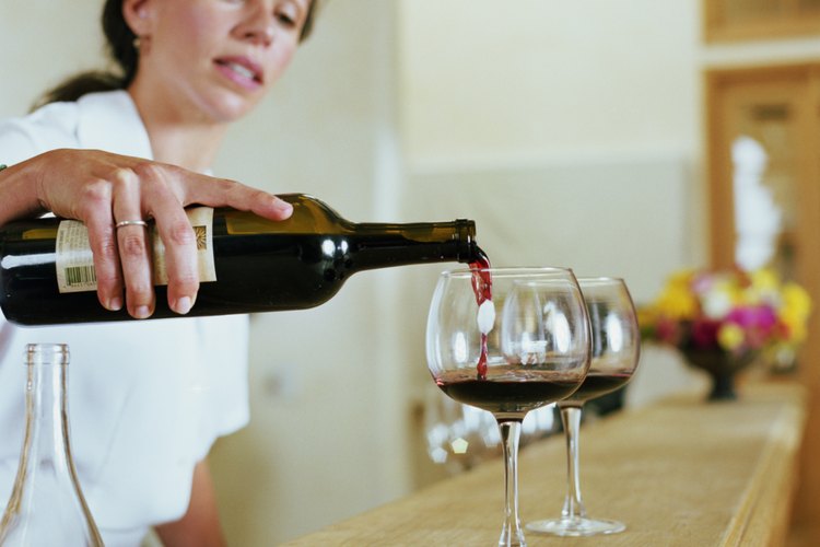 Un camarero de bar sirviendo dos copas de vino tinto en un bar.
