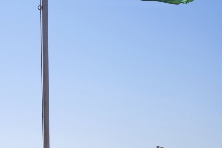 Una bandera blanca flamea cerca de un letrero en la playa.