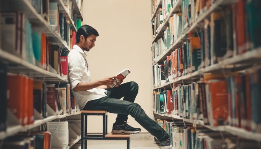 Man sitting and leaning near bookshelf while reading book.jpg