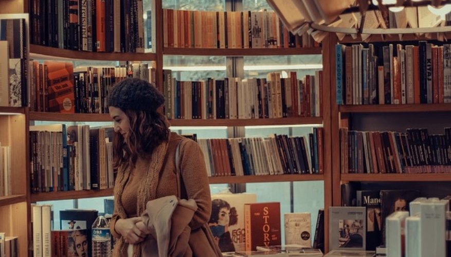 Woman in brown coat reading book in library.jpg