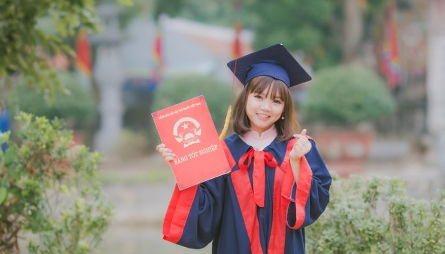 Woman wearing black and red academic dress and mortar board holding red book cover near green grass.jpg
