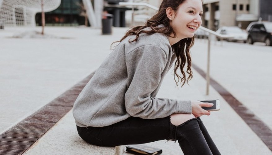 Woman sits on sidewalk holding smartphone while smiling.jpg