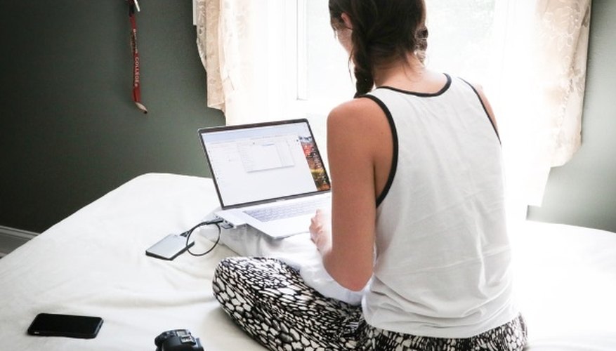 Woman in white tank top sitting on bed in front of laptop computer.jpg