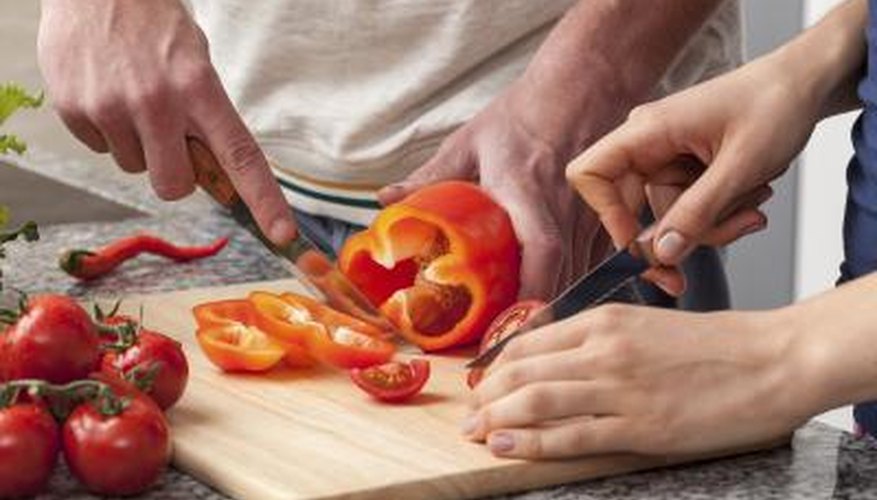 A man and woman sharing a cutting board to chop vegetables together.