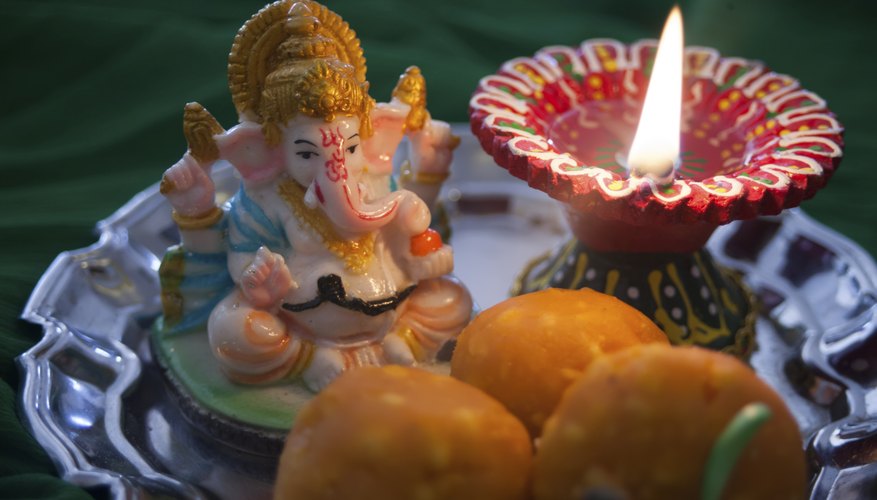 A Ganesh statue, prayer candle, and sweet treats on a plate.