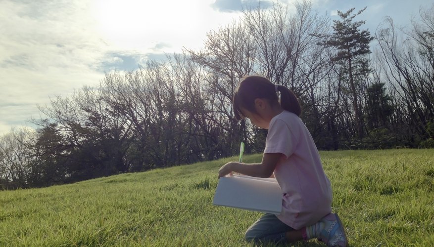 Young girl writing in journal while kneeling on grass.