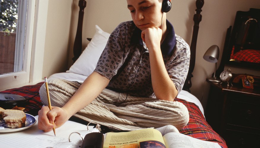 Teenage boy doing homework on his bed.