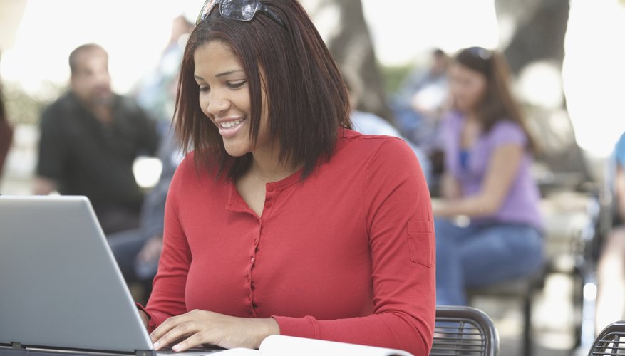 Student writing analysis on laptop with book beside her