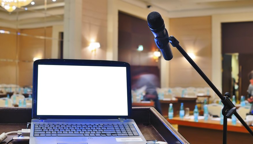 A laptop on a rostrum next to a microphone in a large meeting room.