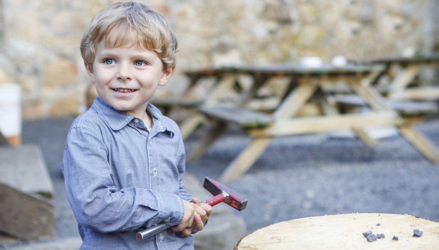 Little boy playing with a hammer outdoors.