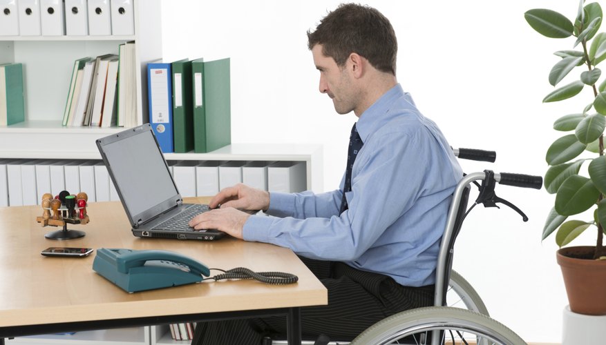 A disabled man sits at his desk in a wheelchair.