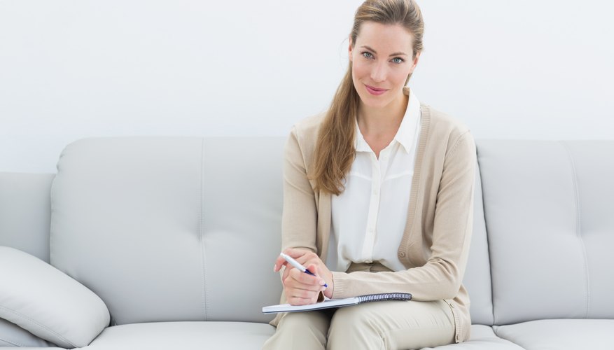 An Adlerian therapist sitting on couch with clipboard in hand.