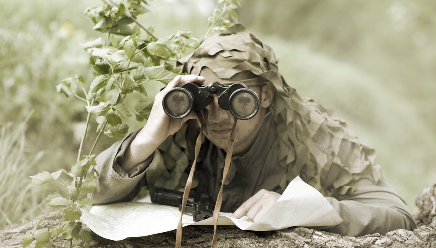 Camouflaged soldier with binoculars and map.