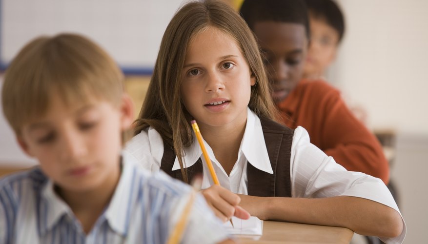 Children writing at desks in classroom.