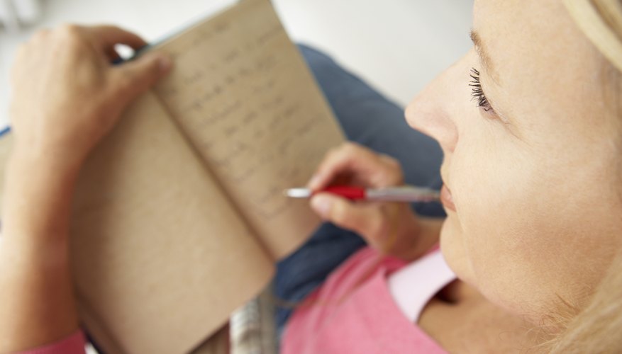 A woman ponders while writing in a notebook.