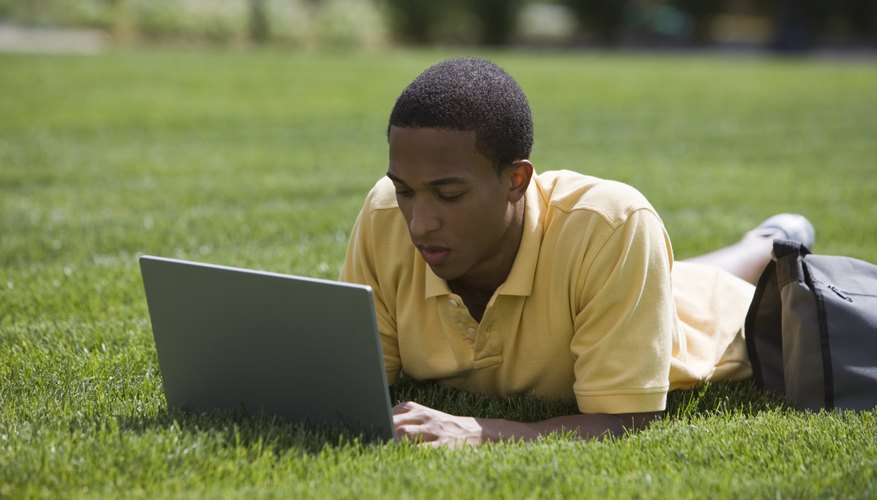 Student working on laptop while lying on grass field