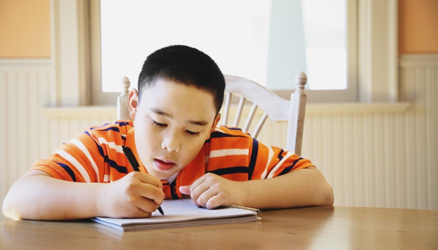 Young boy writing in notebook at kitchen table.