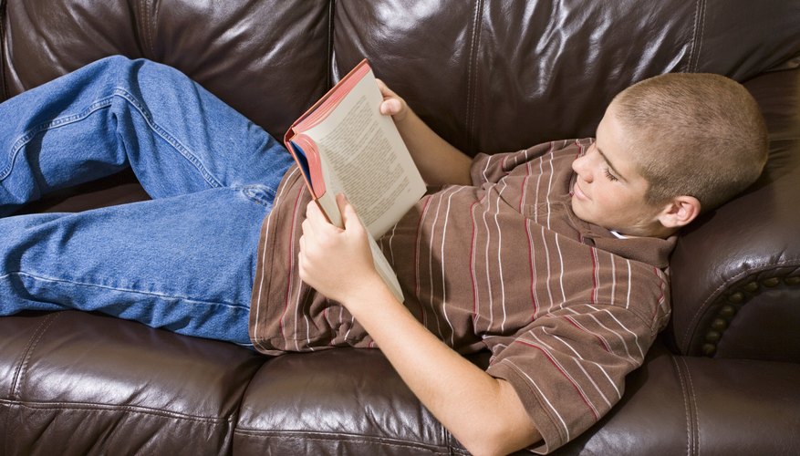 Teenage boy reading a boy on a couch.