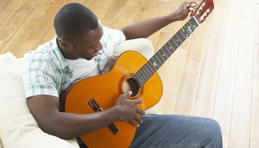 Guitar player tuning guitar on couch.