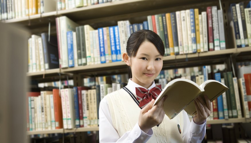High school student holding book open in library.