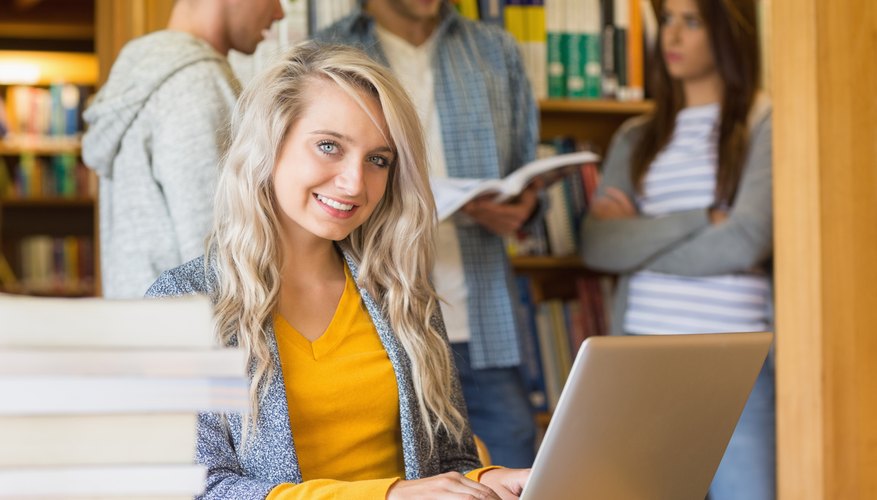 Student on laptop in library with pile of books next to her
