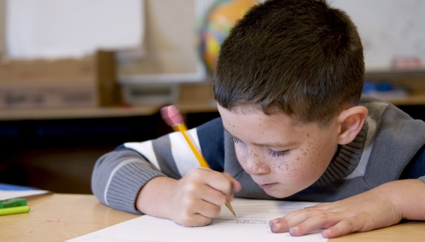 An elementary student writing at a classroom table.