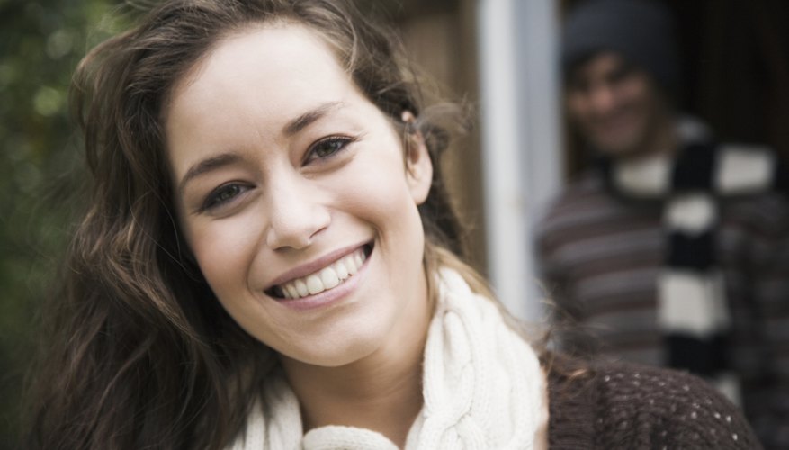 A close-up of a happy woman with a man smiling in the doorway behind her.