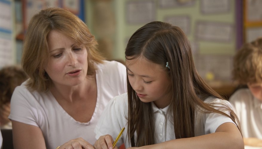 Teacher helping young student sound out a word at her desk
