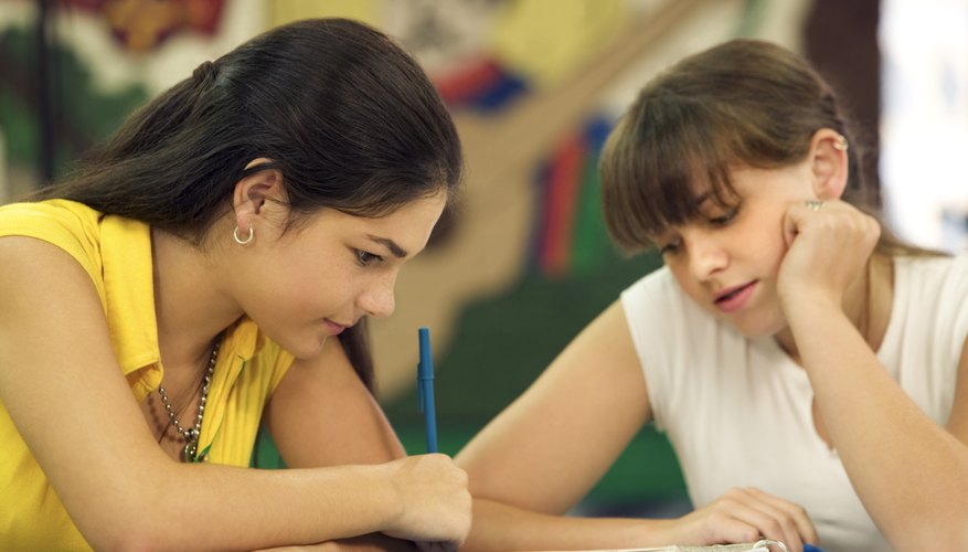 Students writing in notebooks at desk.