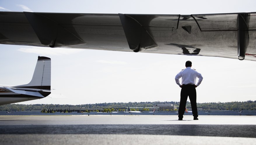 An airline pilot standing on the tarmac under the wing of a plane.