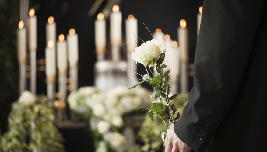 Person holding a rose in front of casket at funeral.