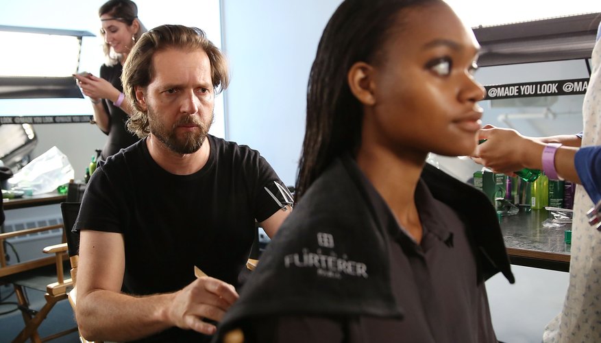 A cosmetologist assessing his client's hair in a salon.