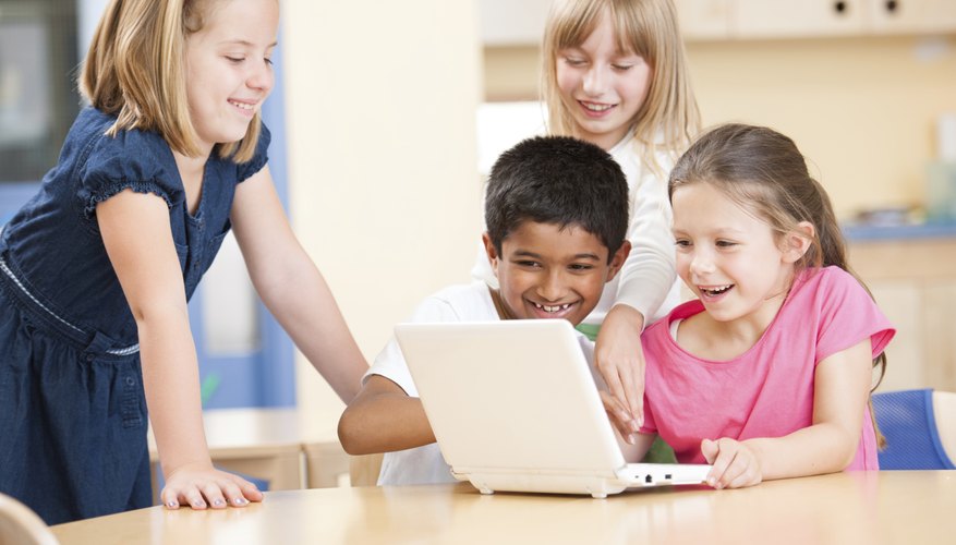 A group of first graders sit around a small learning laptop together