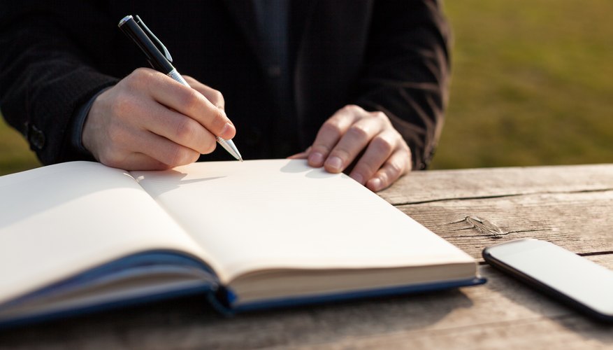 A man writing in a journal at an outdoor table.