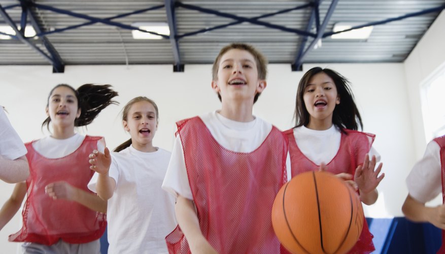 A group of students play basketball in a school gymnasium.