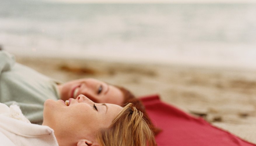Who friends talking to each other while laying next to each other at the beach.
